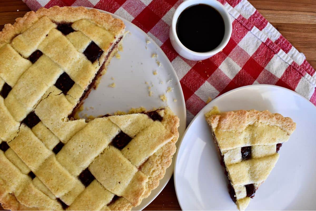 Italian crostata slice on a white plate with a cup of coffee next to it. 