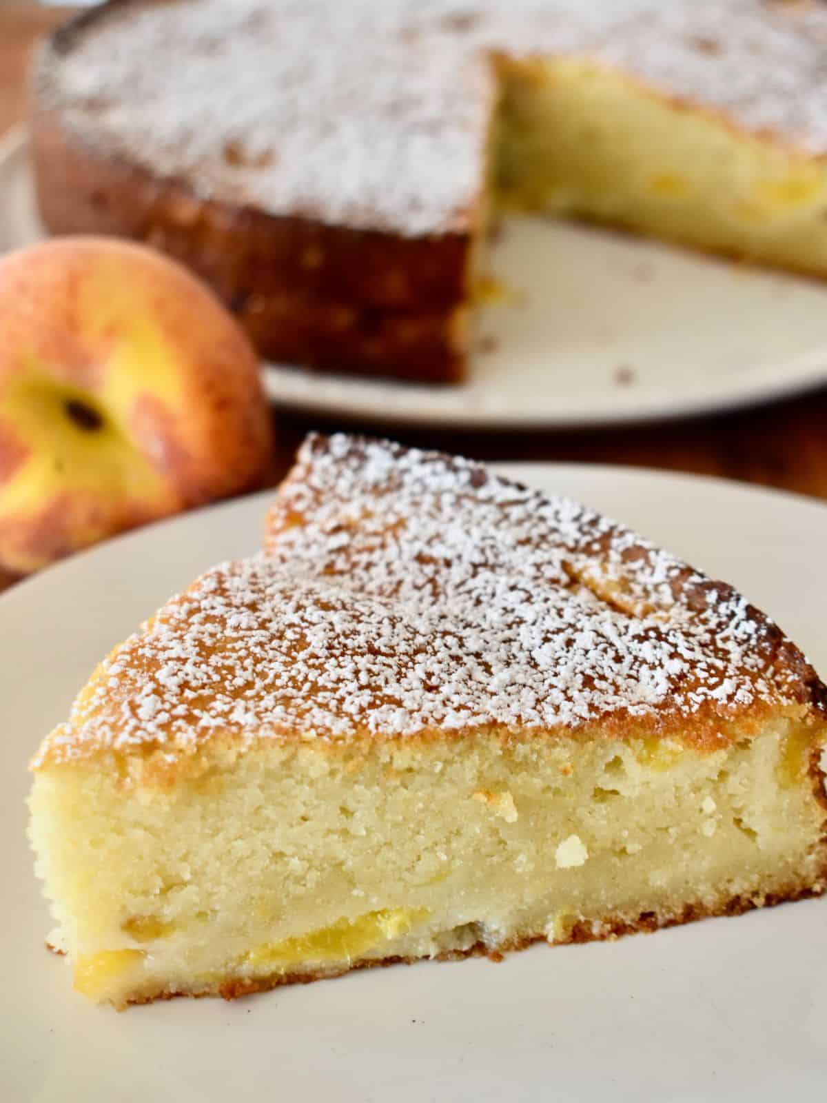 Peach Ricotta Cake on a white plate with a peach behind it. 