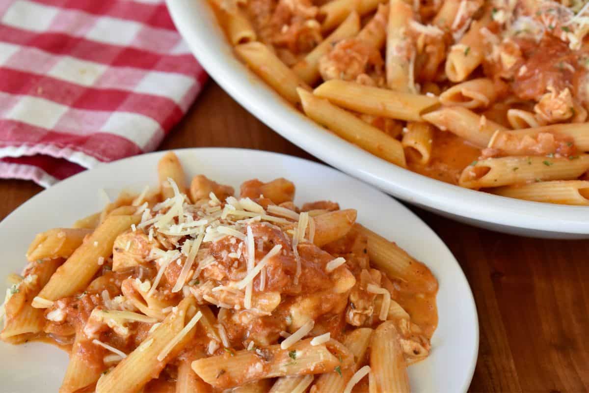 Penne alla vodka with chicken in a white bowl with the serving dish next to it. 