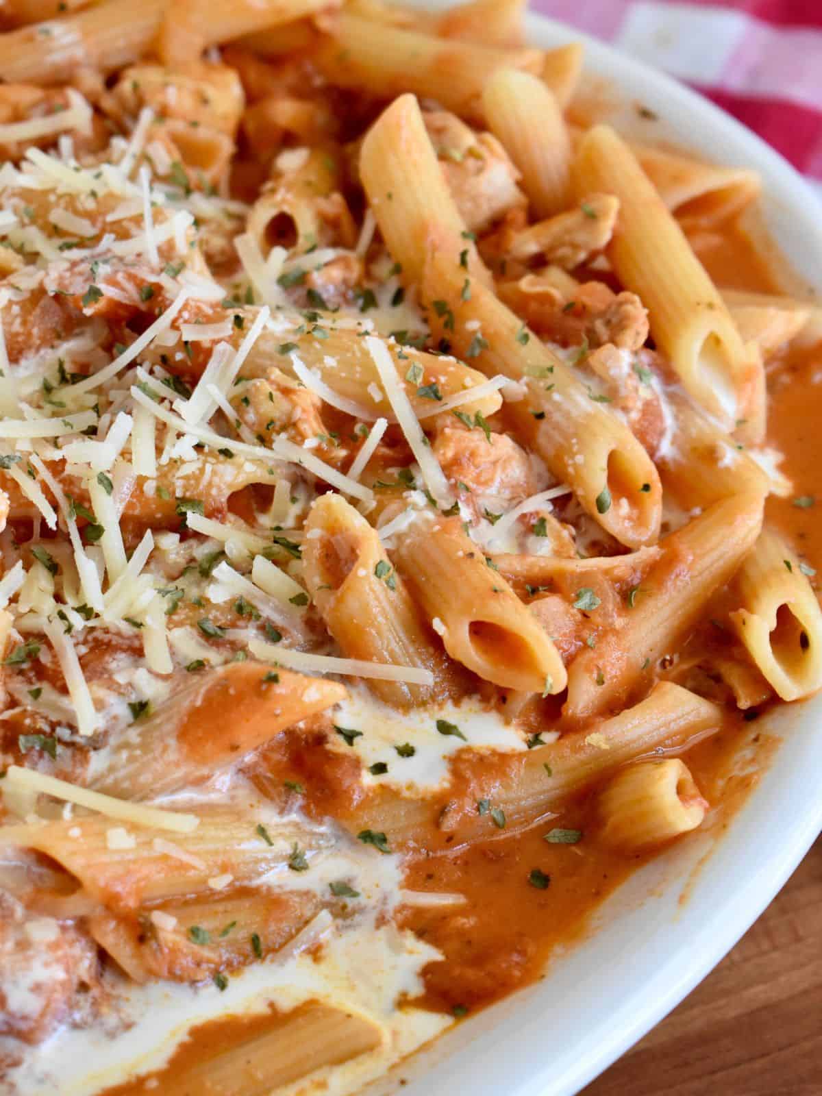 Penne alla Vodka with chicken in a large white serving bowl with parmesan cheese sprinkled on top. 