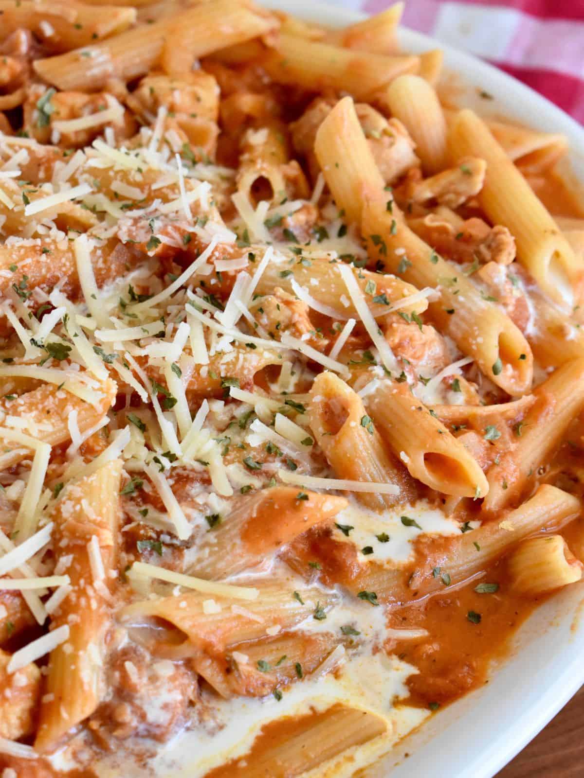 Penne alla vodka with chicken in a large white serving dish with parmesan cheese on top. 
