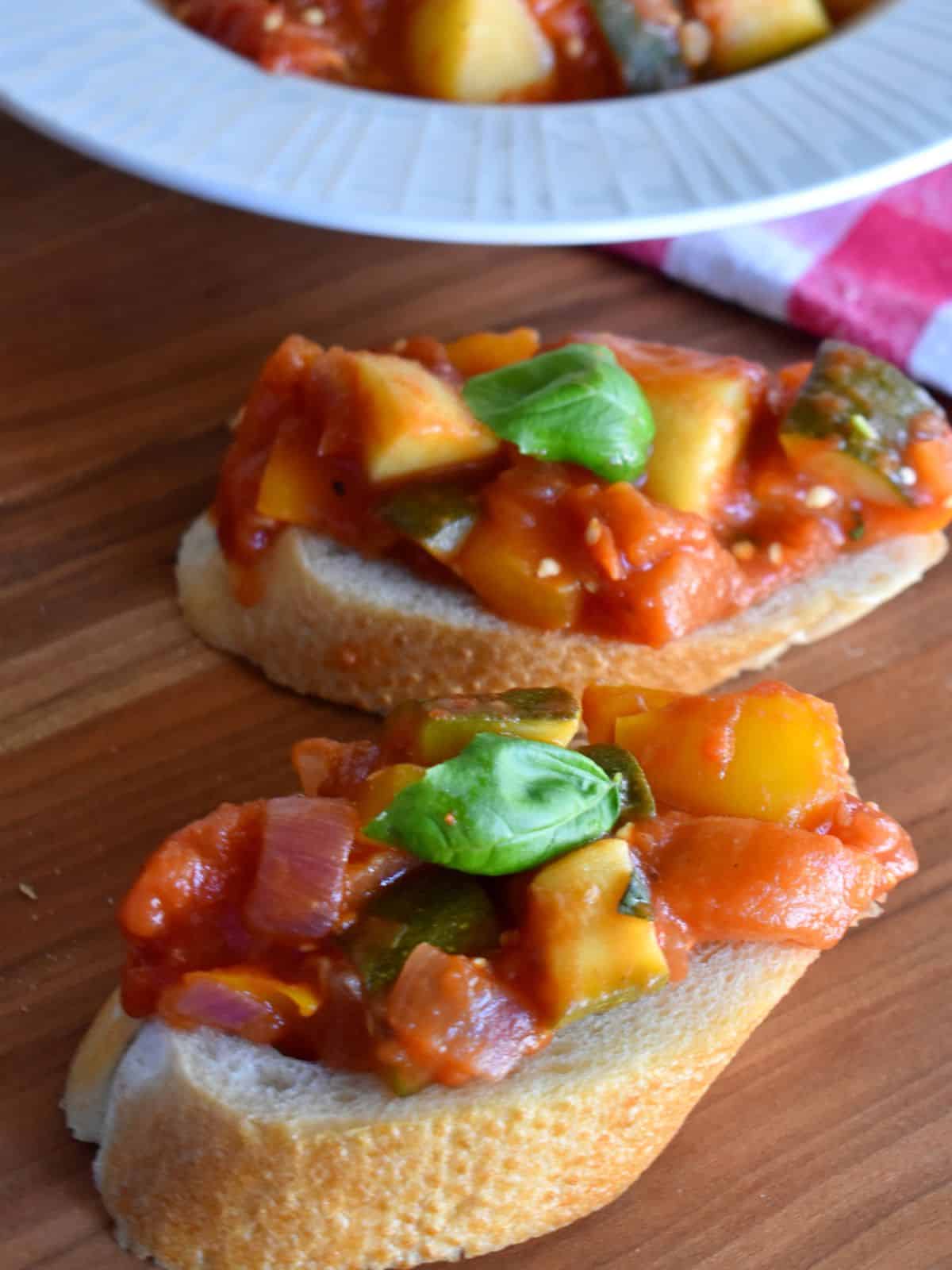 Italian Ciambotta stew on top of pieces of sliced bread with a basil leave on top. 