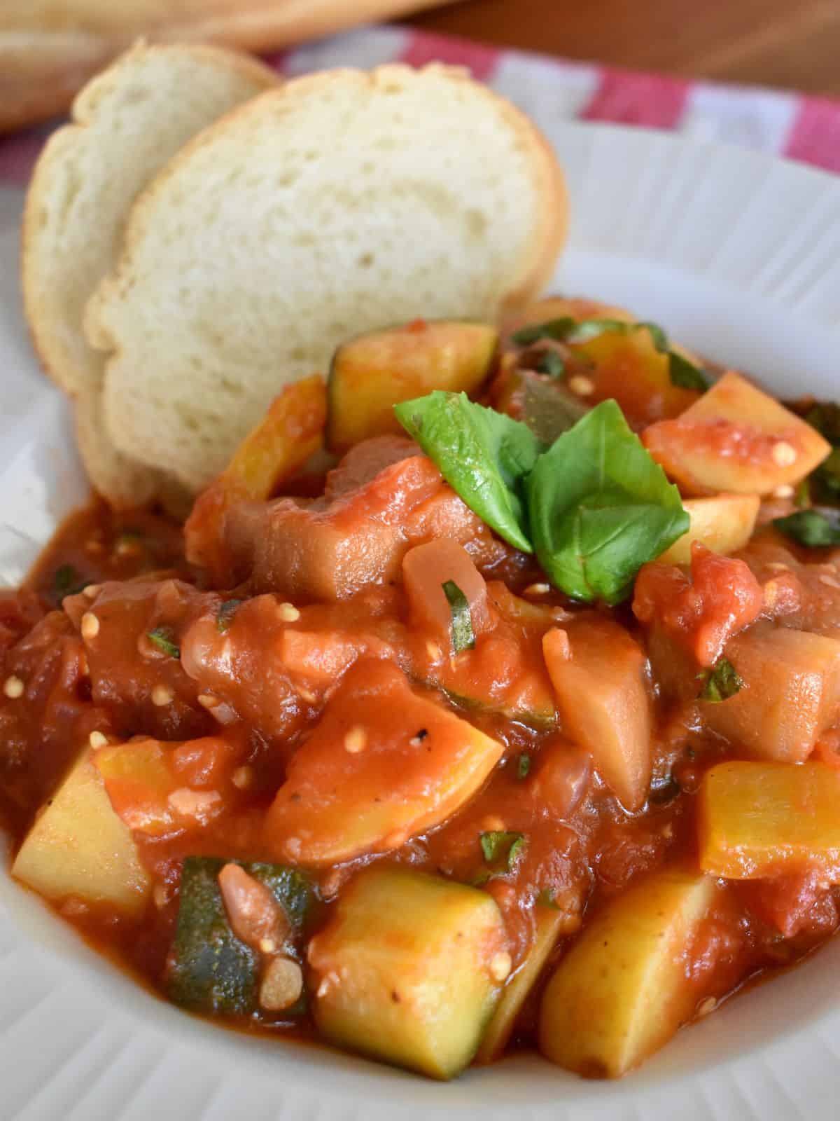 Ciambotta in a white bowl with bread. 