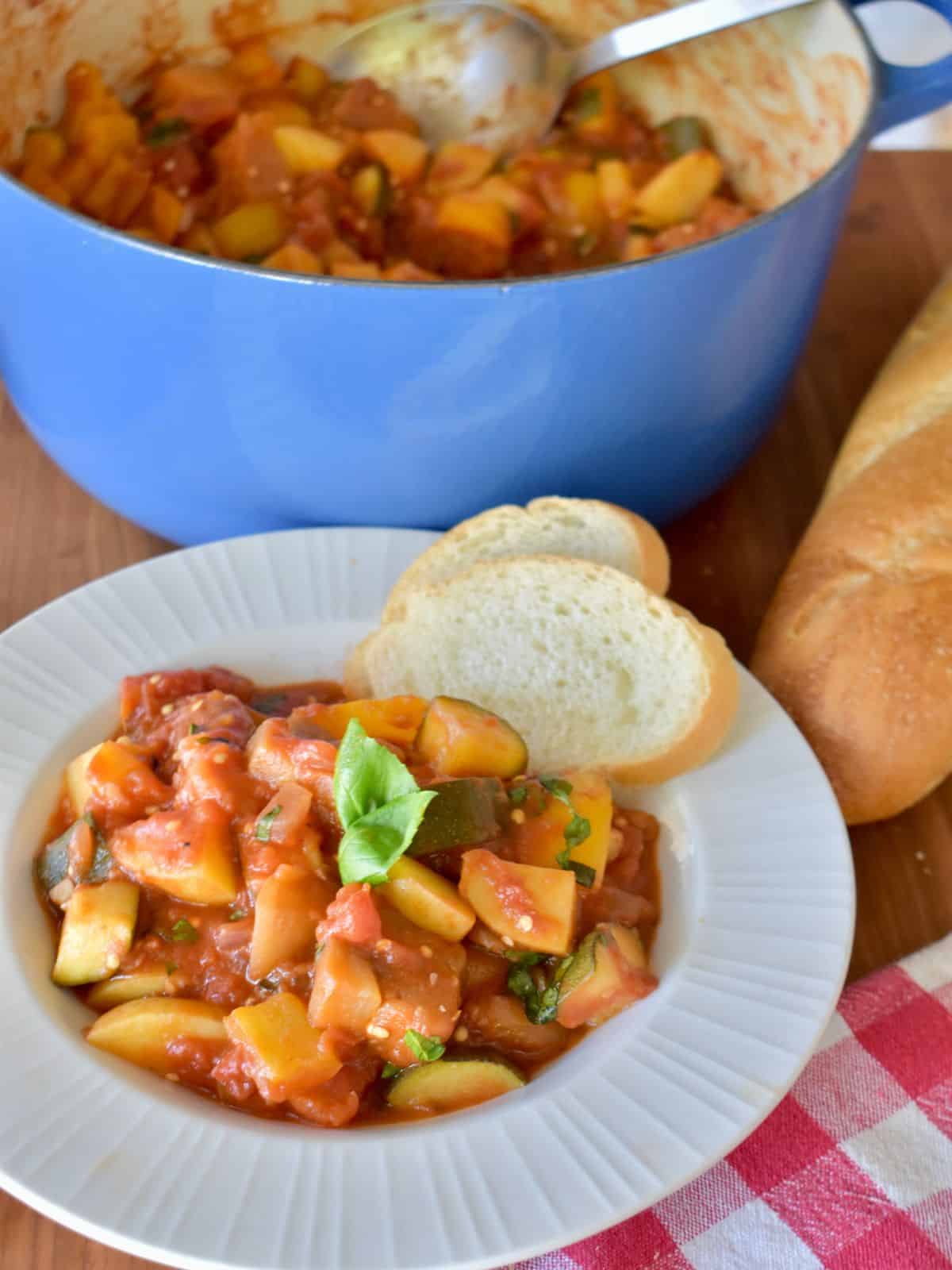 Ciambotta in a white bowl with a blue pot of the stew in the background. 