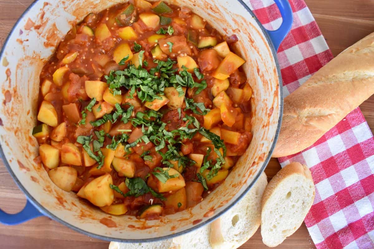 Ciambotta Italian summer vegetable stew in a blue pot with bread next to it. 