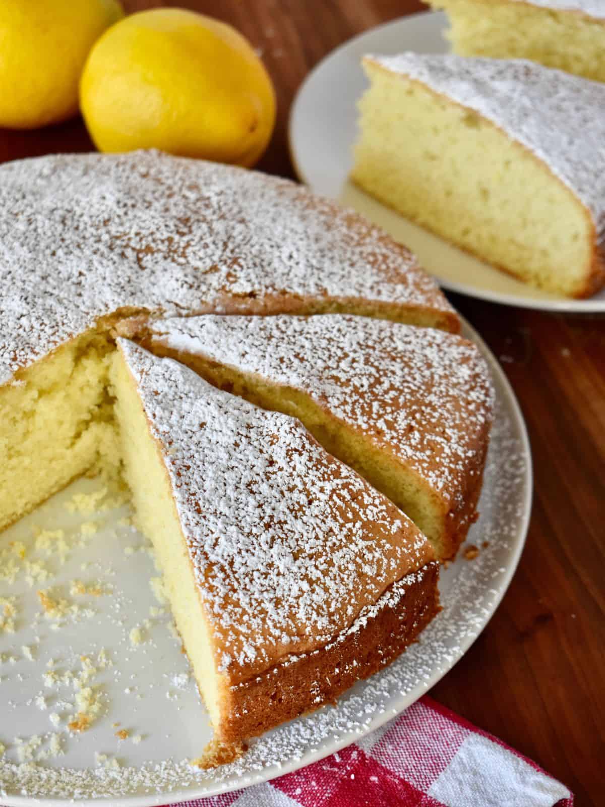 Torta Paradiso on a white place sliced with lemons in the background. 