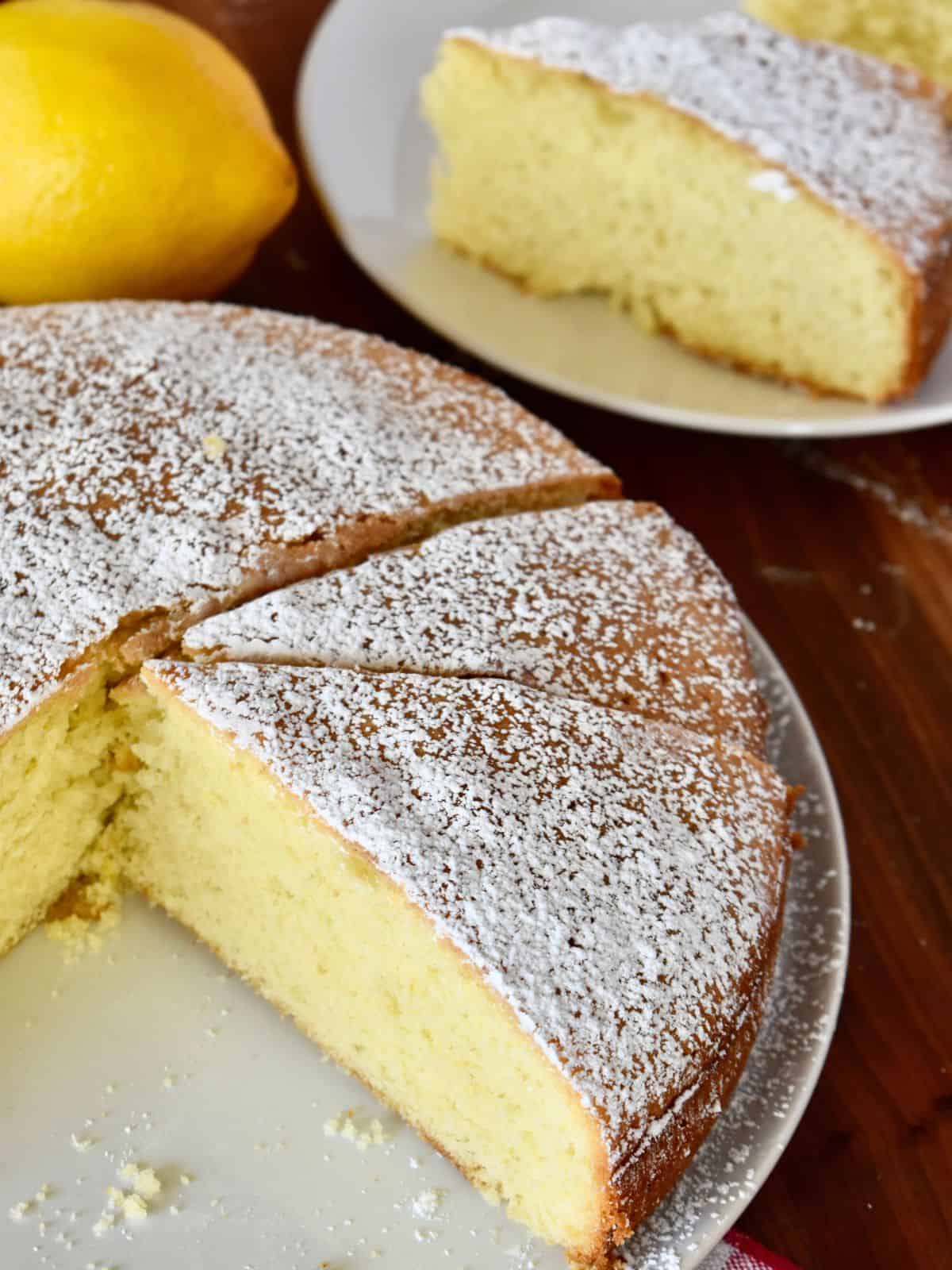 Italian Paradise Cake on a white plate dusted with powdered sugar and lemons in the background. 