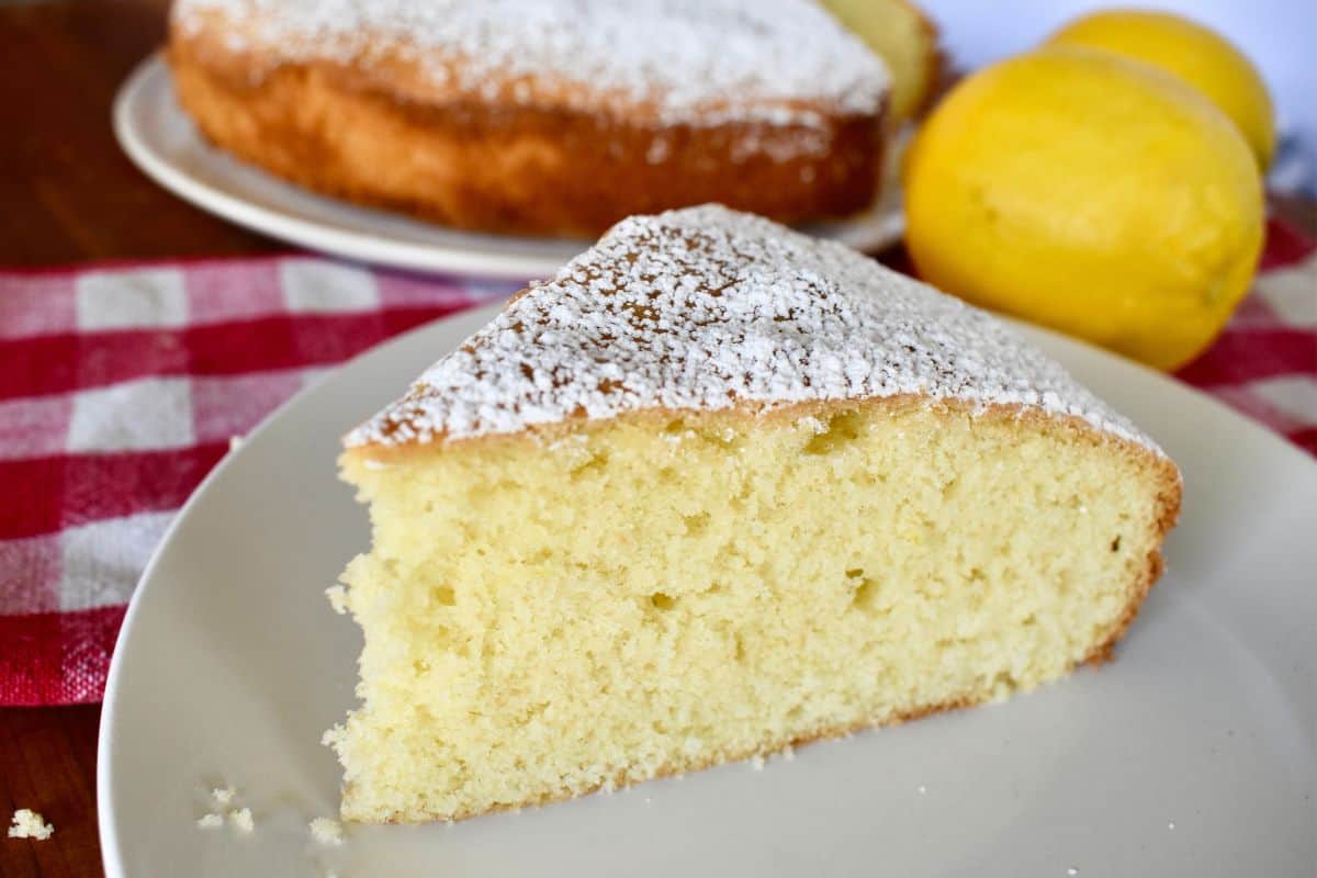 Slice of Italian paradise cake on a white plate with a lemon in the background.