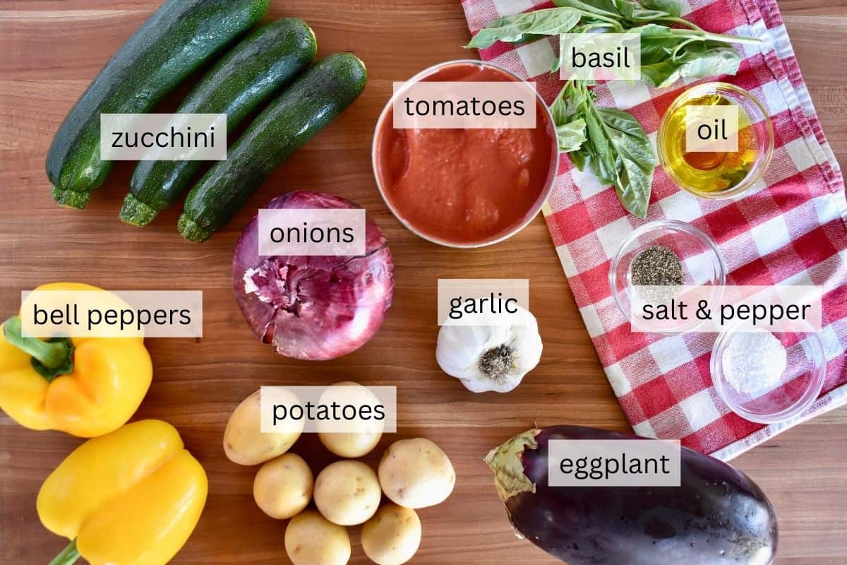 Ingredients for Italian summer vegetable stew including zucchini, eggplant, potatoes, bell peppers, garlic, onion, tomatoes, and basil. 