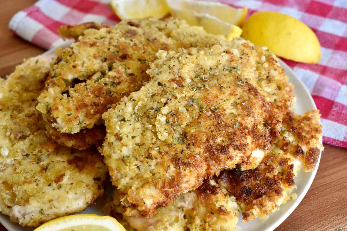 Italian Chicken Cutlets on a white plate with a red checkered napkin in the background. 