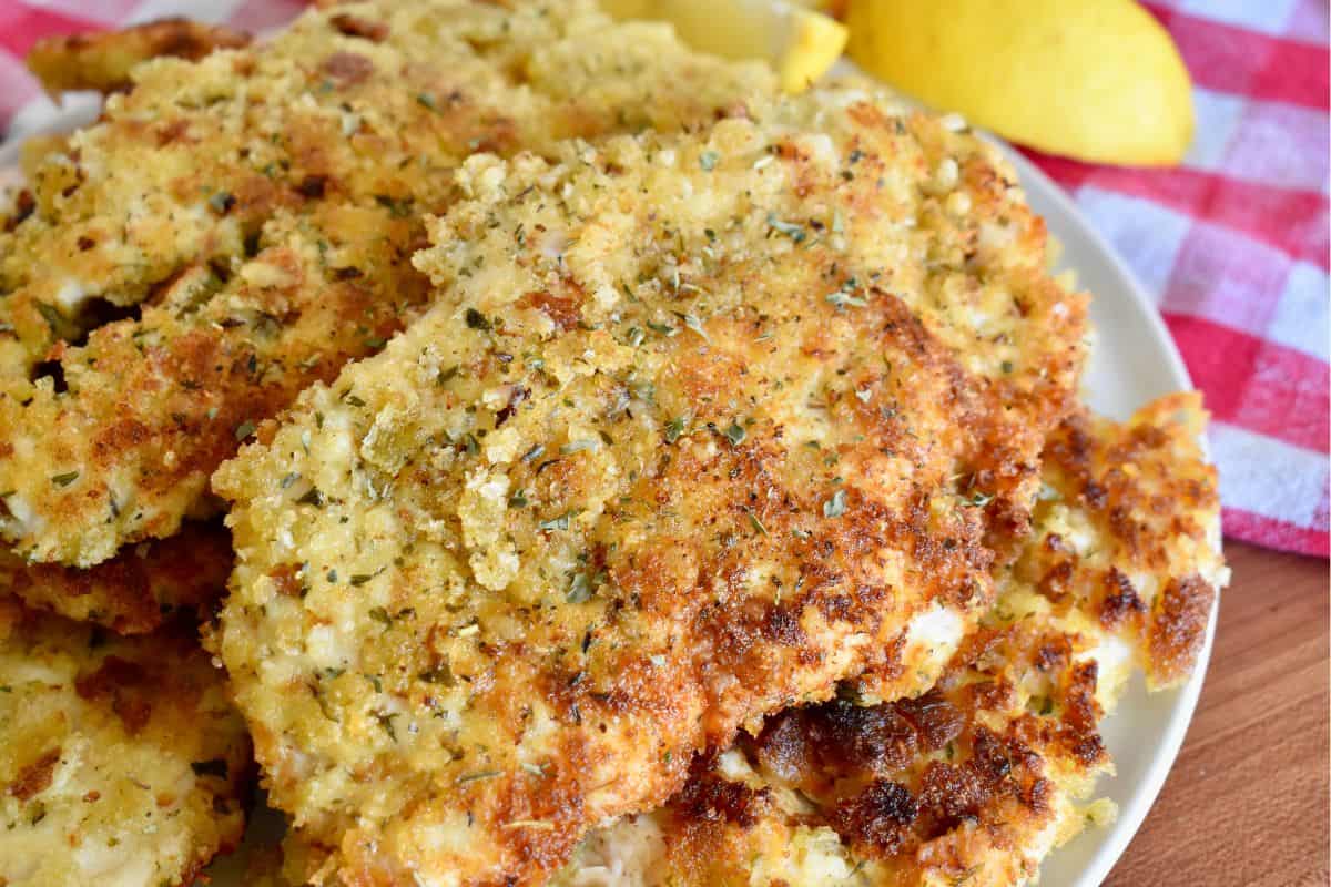 Italian Chicken Cutlets on a white plate with a red checkered napkin in the background. 