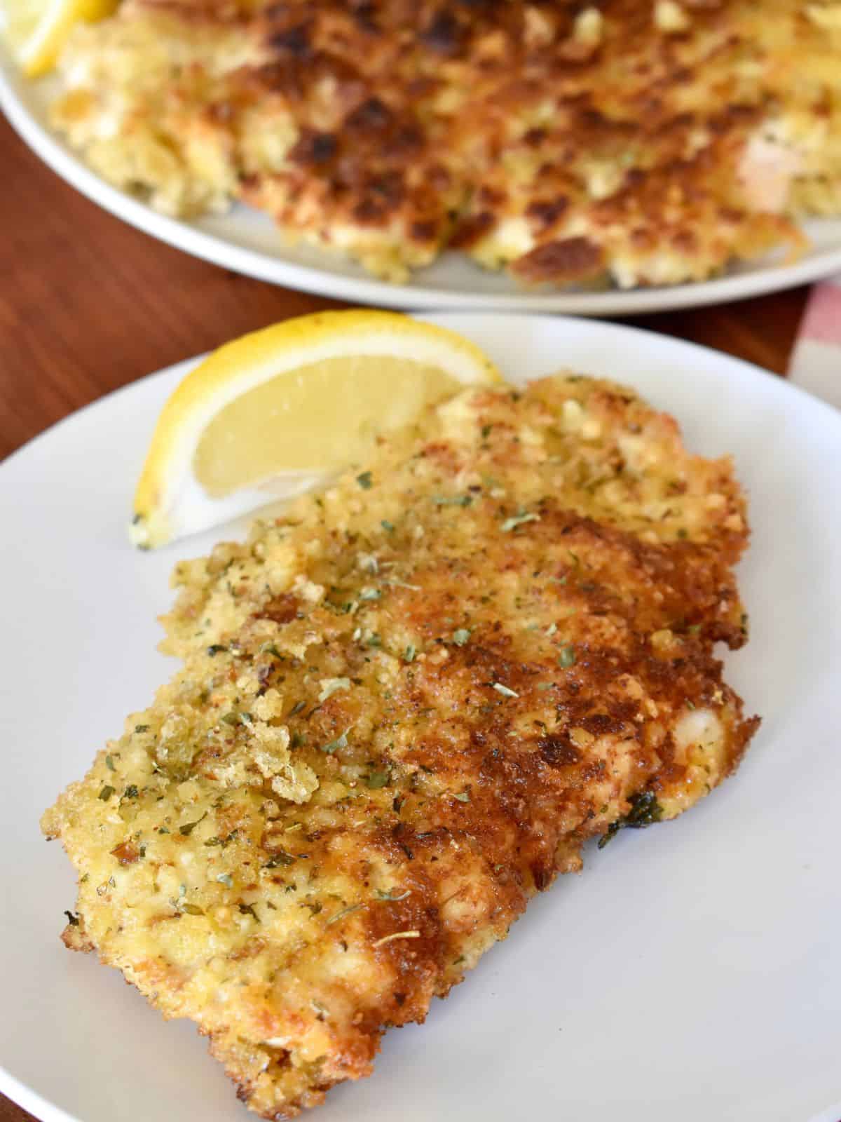 Italian Chicken Cutlets on a white plate with a lemon wedge. 