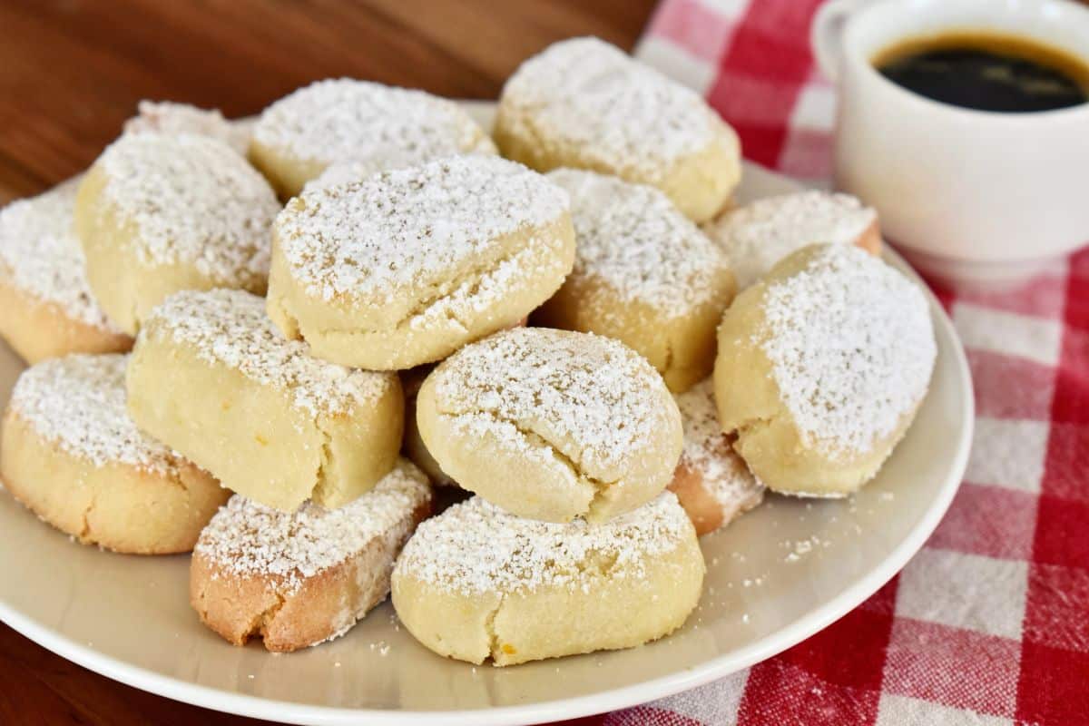 Ricciarelli Italian almond cookies dusted with powdered sugar on a white plate with a checkered napkin underneath. 