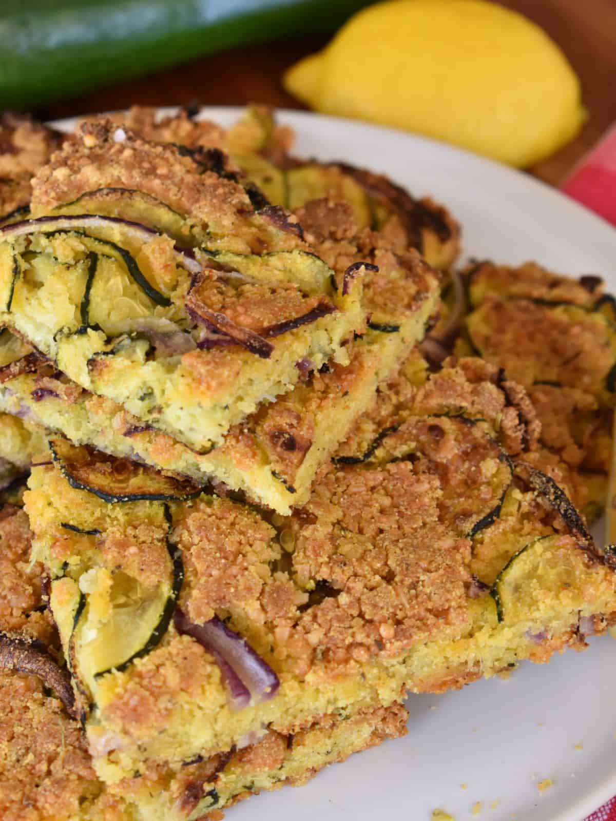 Italian Scarpaccia stacked on each other on a white plate with zucchini and lemon in the background. 