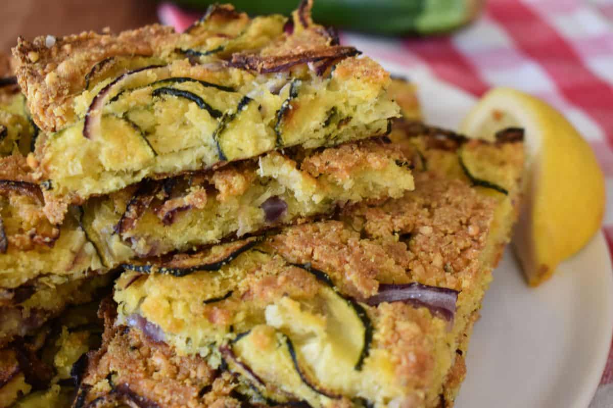 Zucchini Scarpaccia piled on a white plate with lemon wedges. 