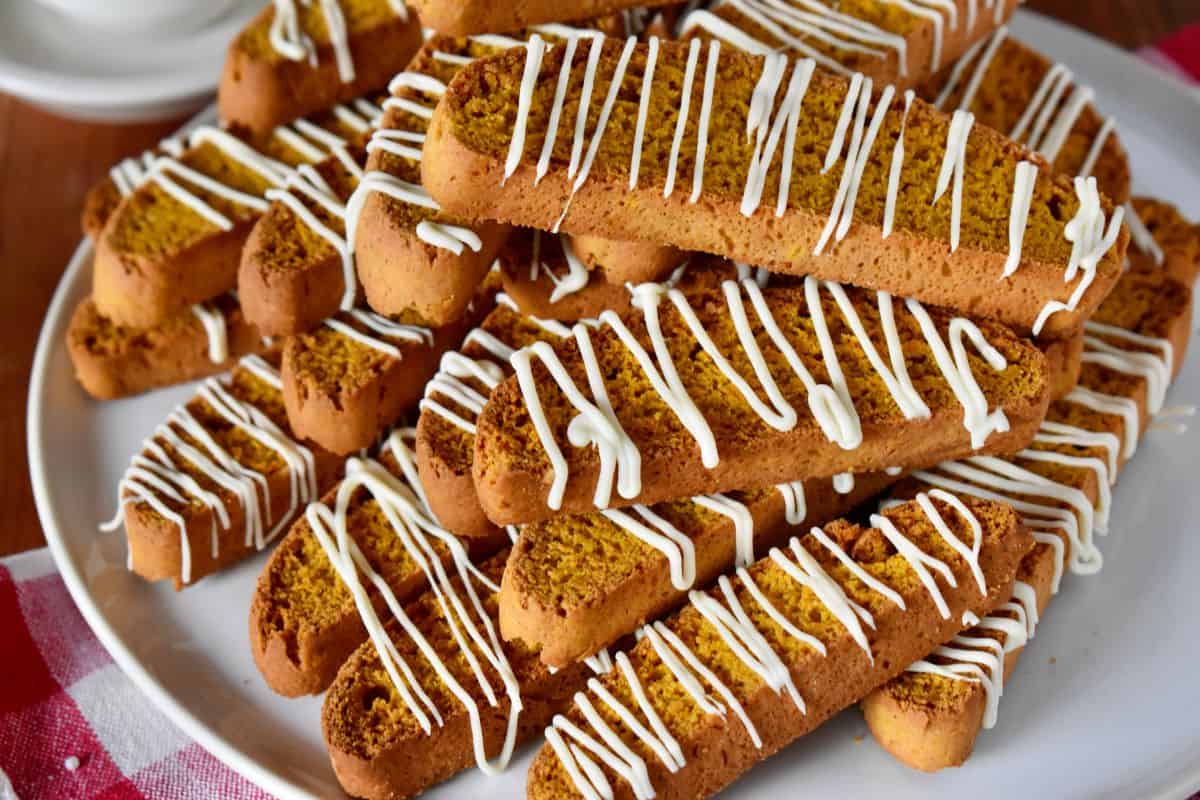Pumpkin biscotti with white chocolate drizzle on a white plate. 