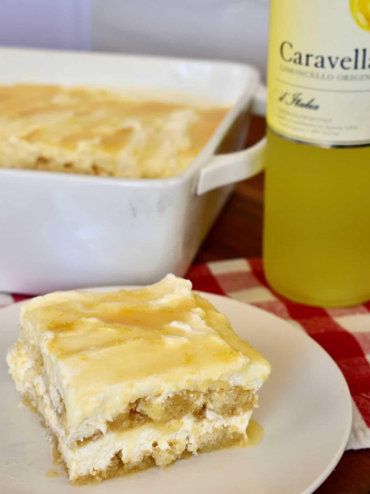 Slice of limoncello tiramisu on a white plate with a bottle of Italian Limoncello liqueur in the background. 