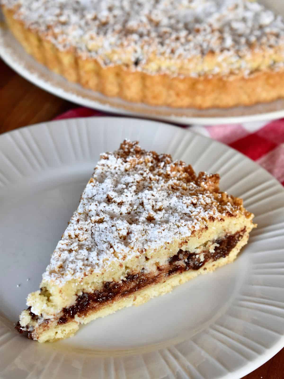 Slice of ricotta crostata on a white plate with the tart in the background. 