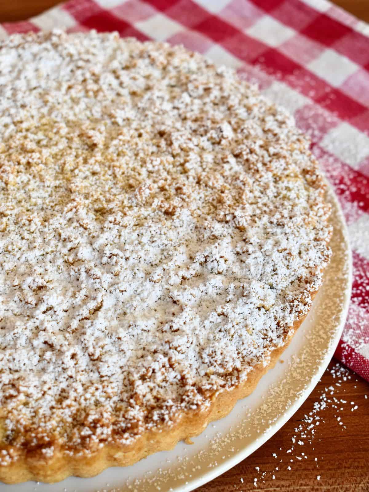 Powdered sugar sprinkled on top of the cooled ricotta crostata on a white plate. 