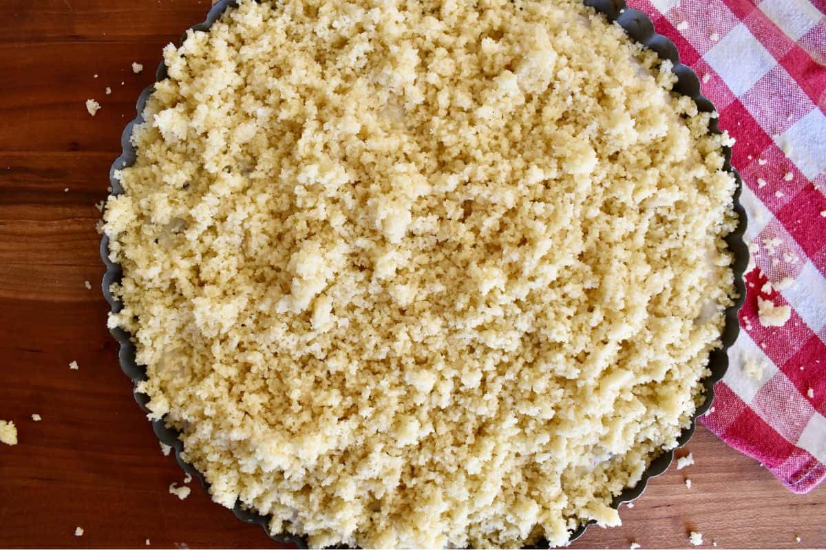 Crumbled pasta frolla dough on top of the ricotta filling in the tart pan. 