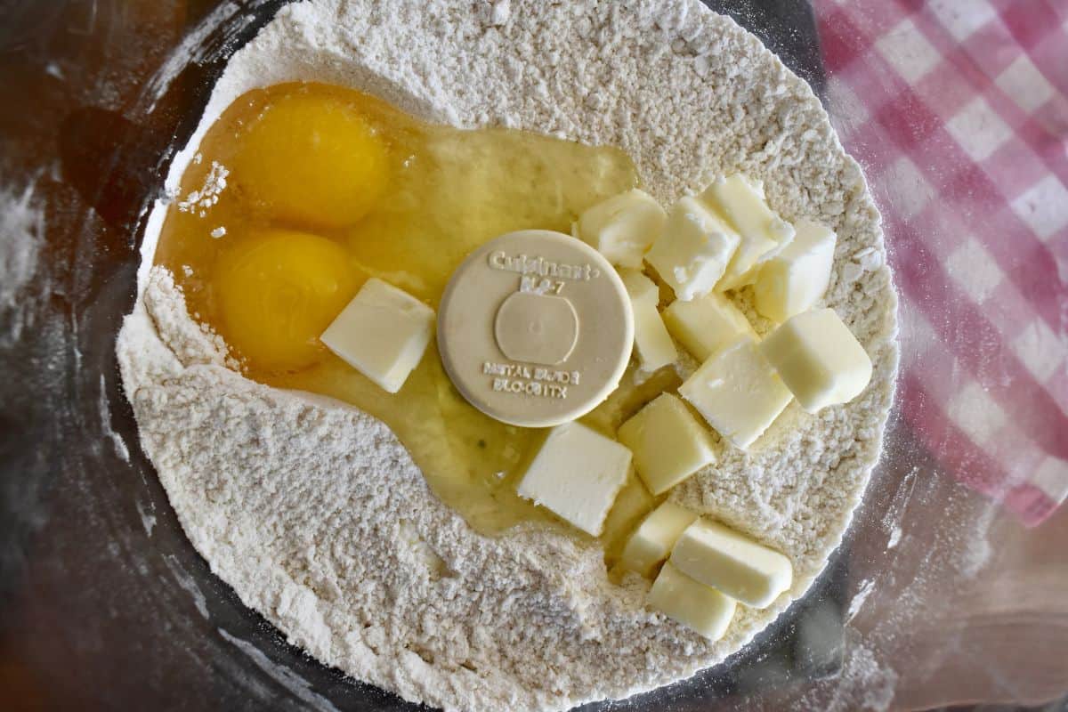 Food processor with flour, sugar, eggs, and butter in it. 