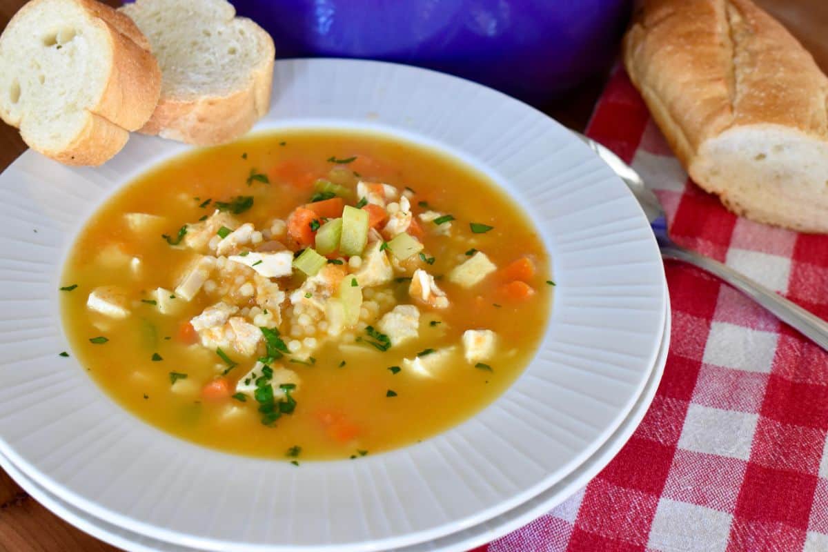 Bowl of Chicken Pastina Soup also known as Italian penicillin, in a white bowl with sliced bread next to it. 