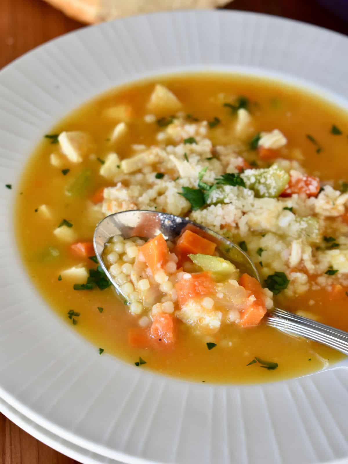 White bowl of chicken pastina soup with a soup.