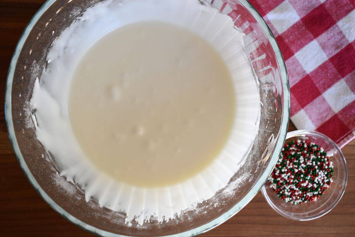 Frosting in a glass bowl with red and green sprinkles next to it. 