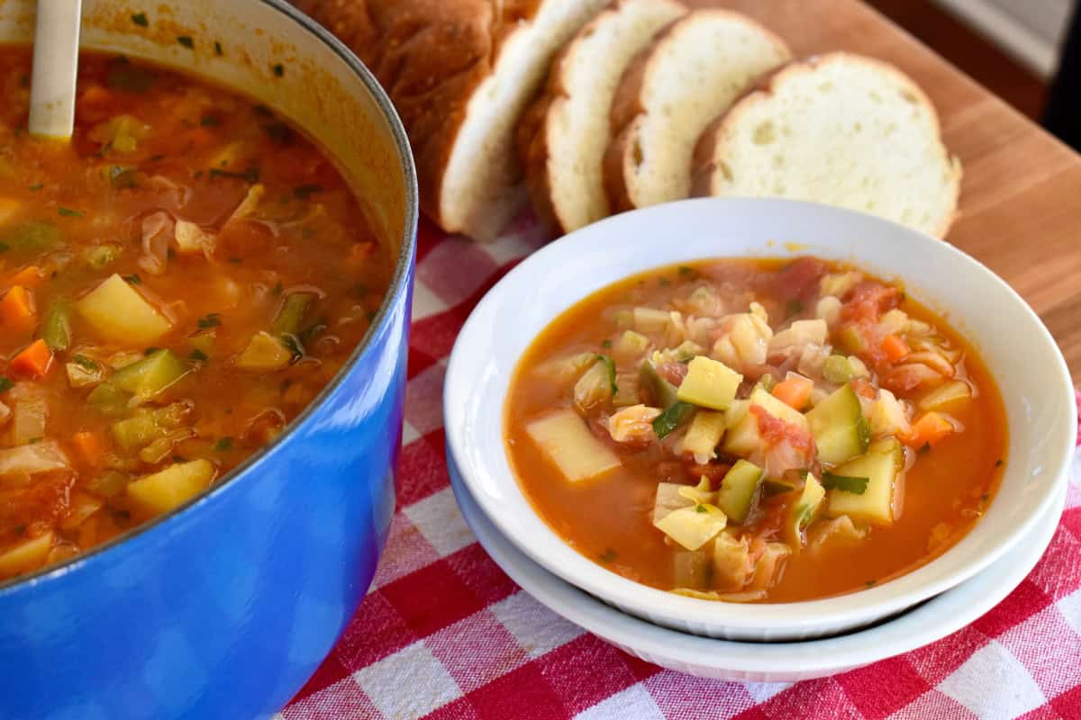 Italian Vegetable Soup in a white bowl with a pot of soup next to it. 