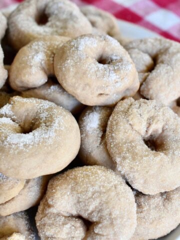 Italian Wine Cookies stacked on a white plate with a checkered napkin in the background.