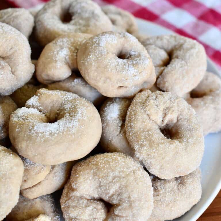 Italian Wine Cookies stacked on a white plate with a checkered napkin in the background.