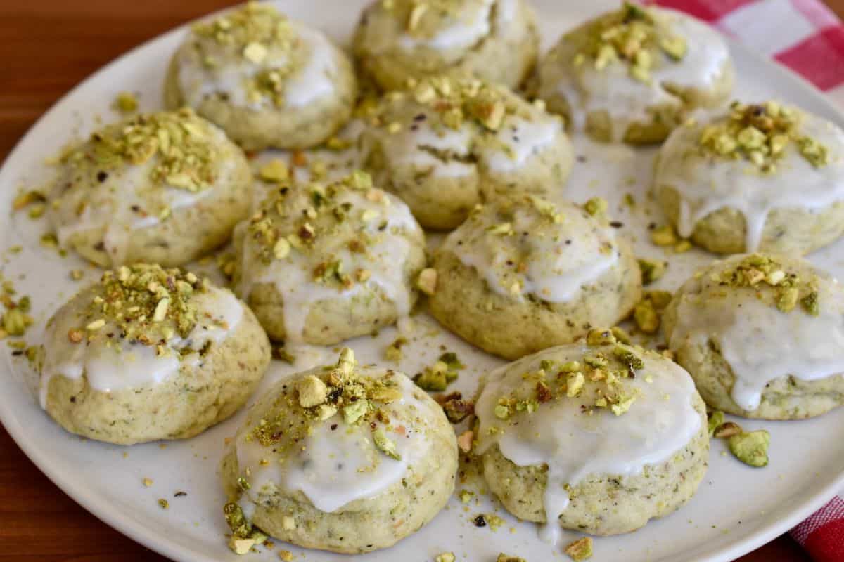 Frosted pistachio ricotta cookies on a white plate. 