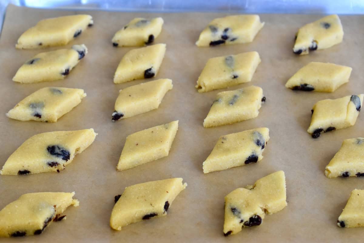 Diamond-shaped Venetian cornmeal and raisin cookies on a lined baking sheet. 