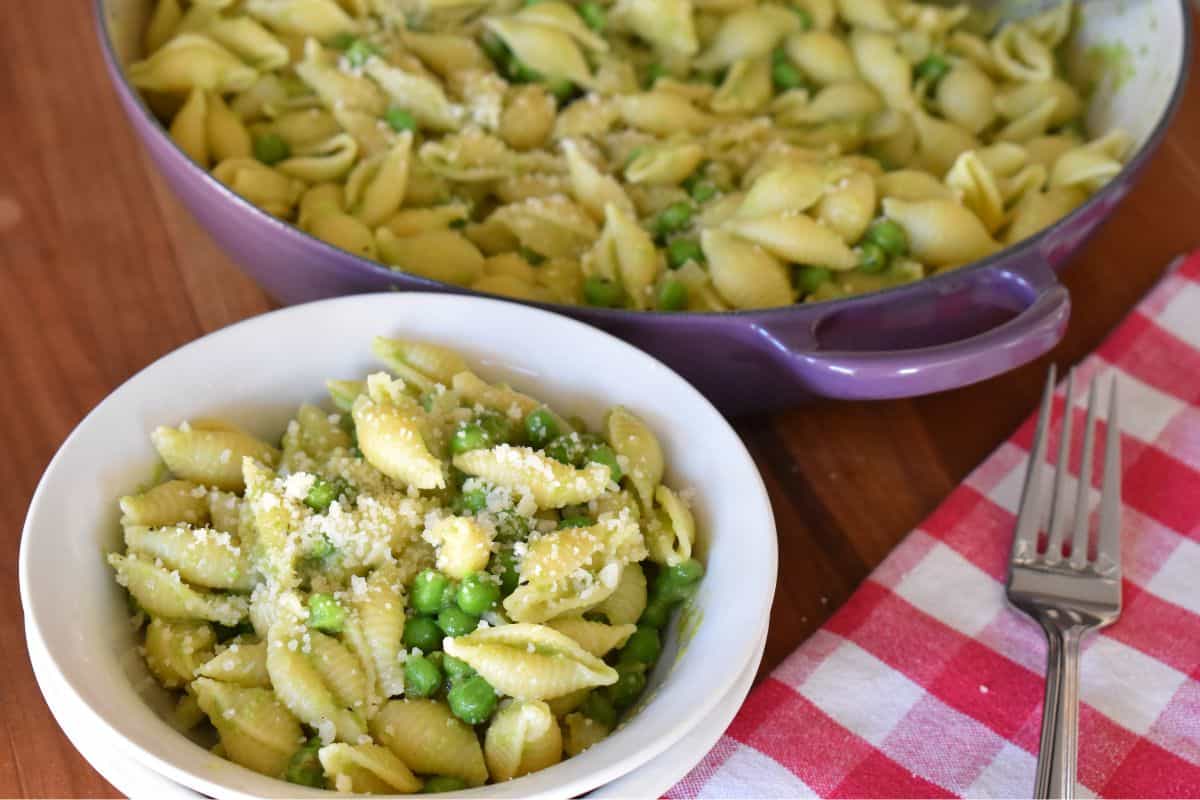 White bowl filled with pasta with peas and topped with grated parmesan cheese. 