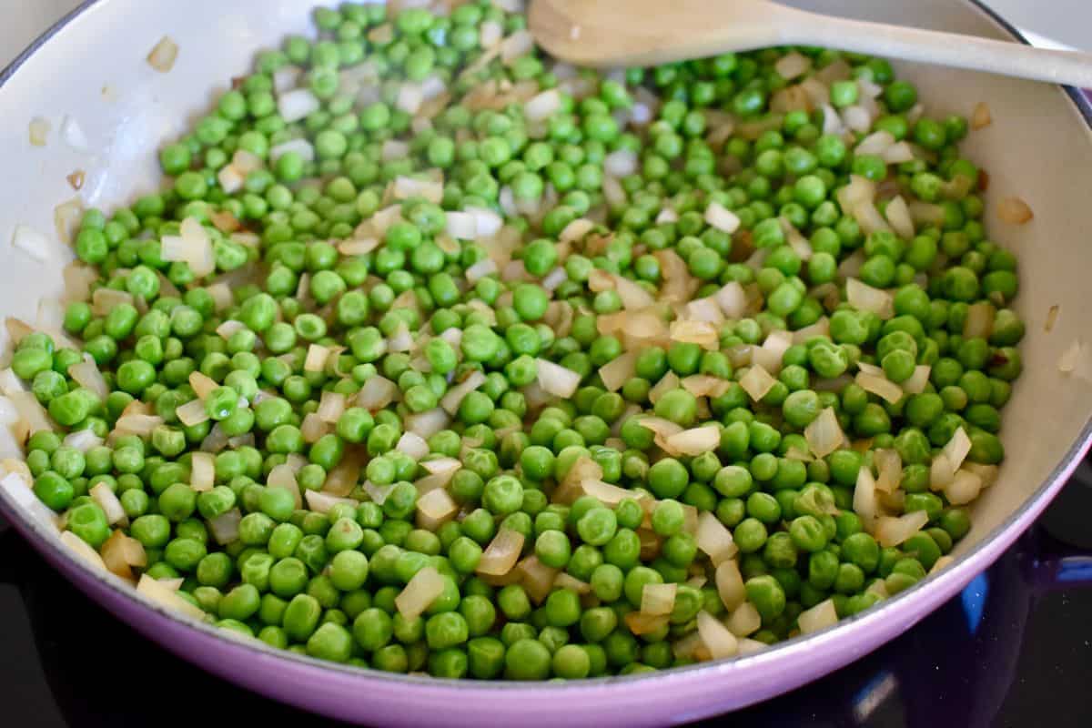 Onions and peas cooking together in a large dutch oven skillet. 