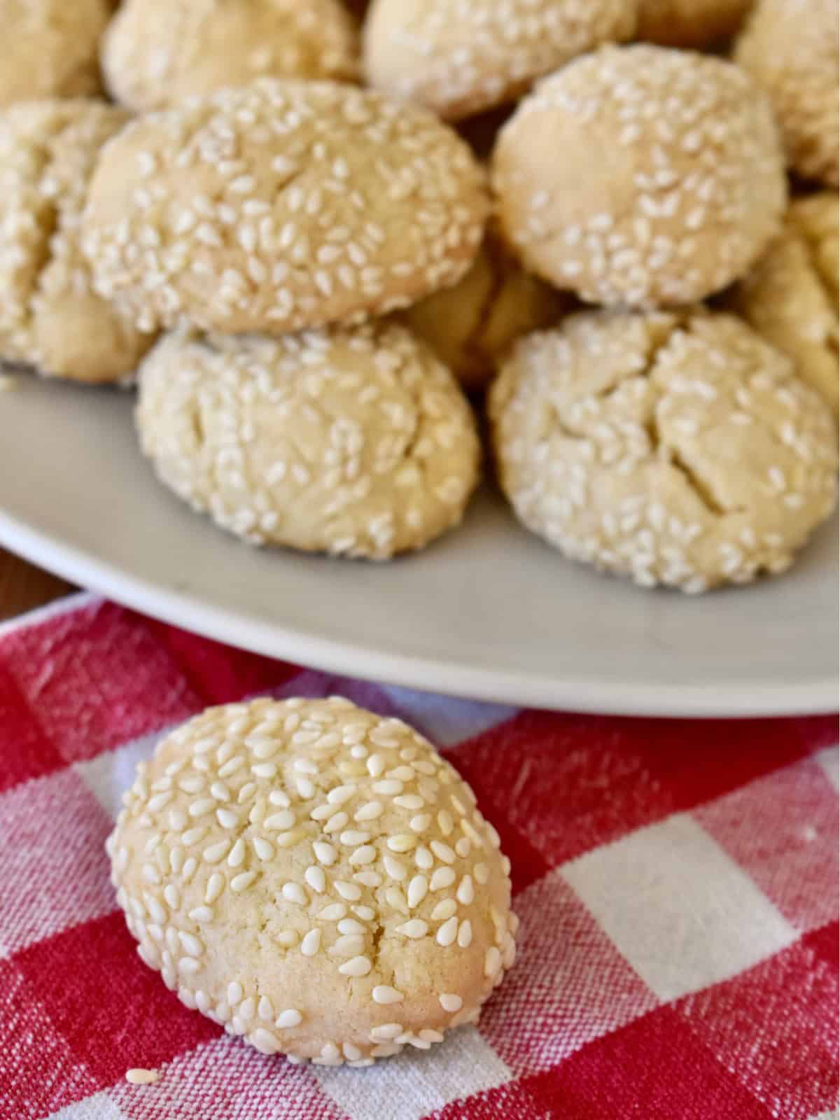 Italian sesame cookies on a white plate with a checkered napkin underneath. 