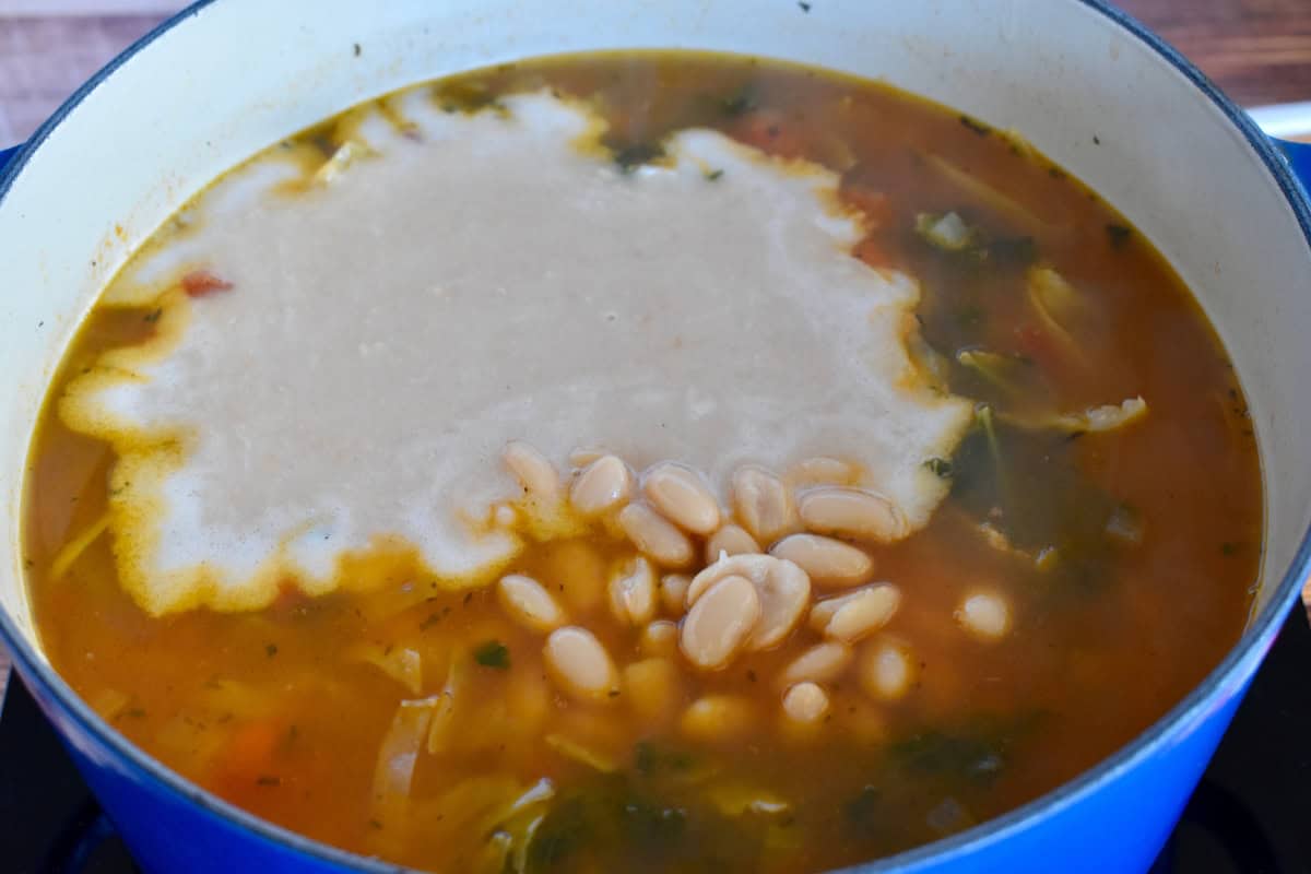 Crushed cannellini beans and whole cannellini beans added to the soup pot. 