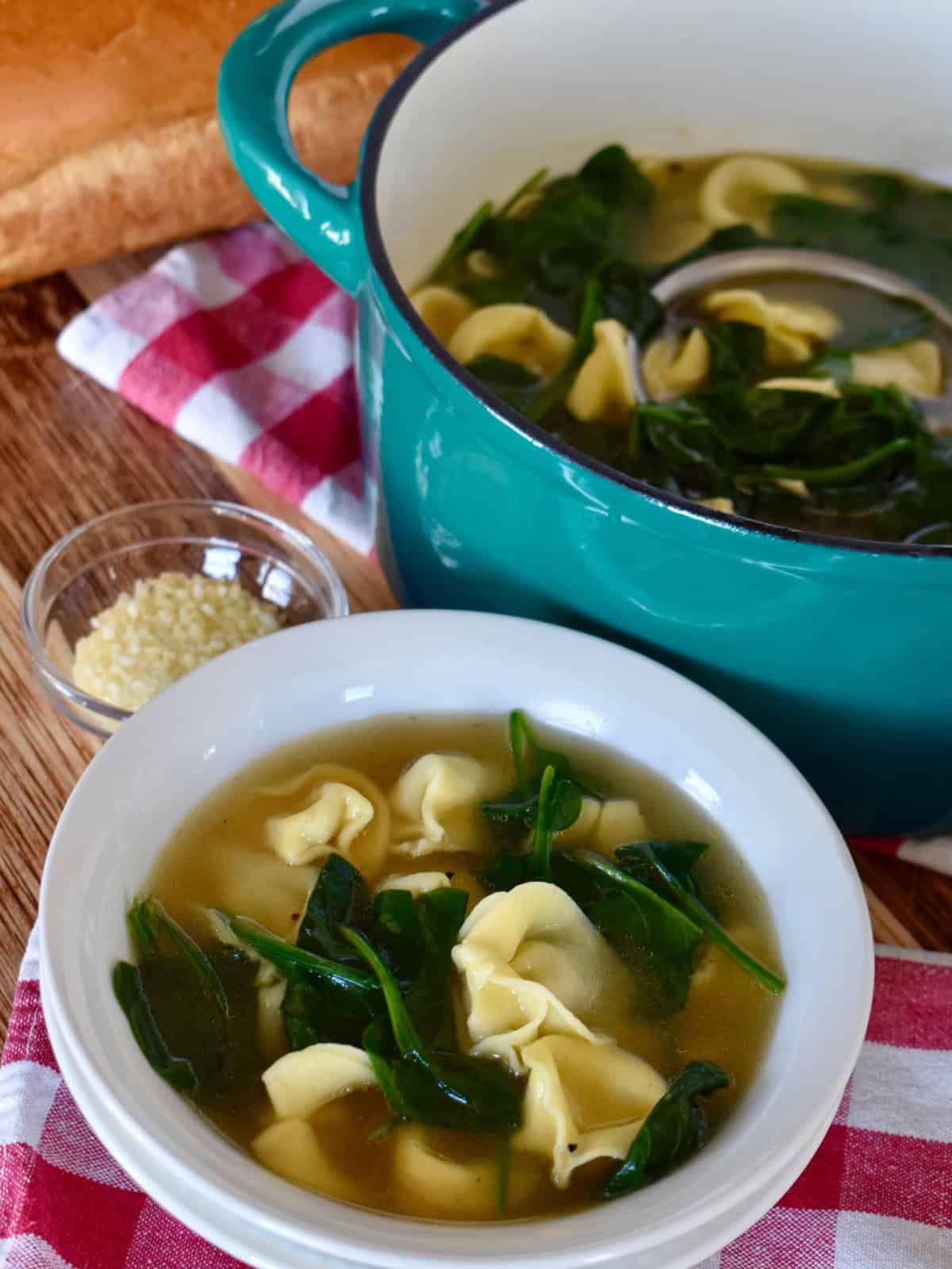 Tortellini en Brodo in a white bowl with a dutch oven full of soup behind it. 