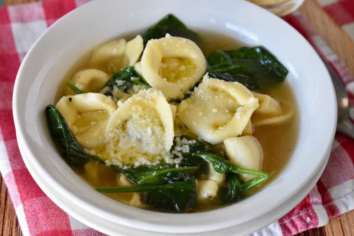 Tortellini en Brodo in a white bowl with a checkered napkin underneath. 