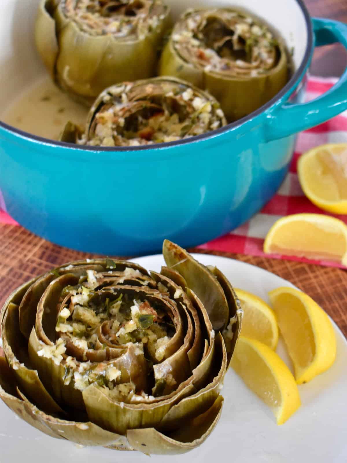 Italian Stuffed Artichokes on a white plate with lemon wedges. 