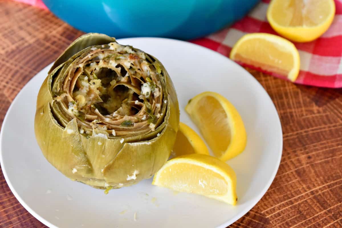 Italian stuffed artichokes on a white plate with lemon wedges. 