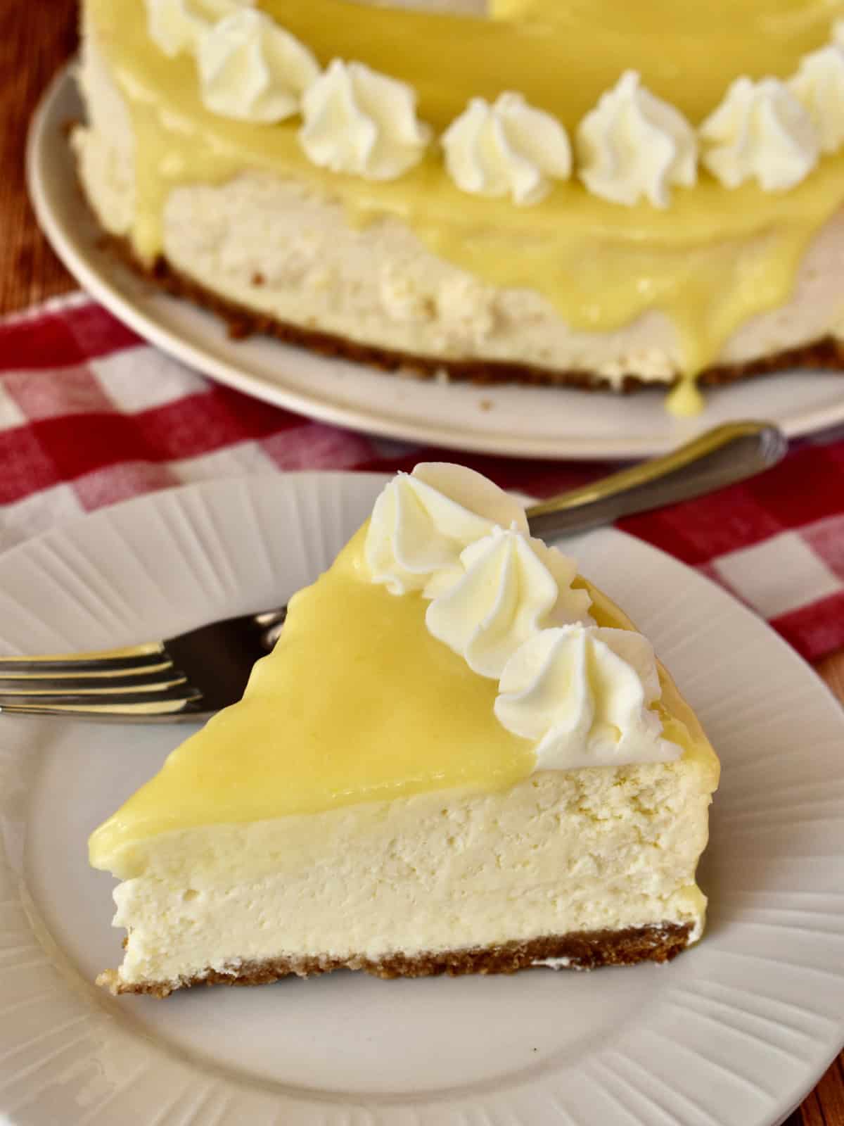 Lemon Ricotta Cheesecake slice on a plate with cheesecake in the background.