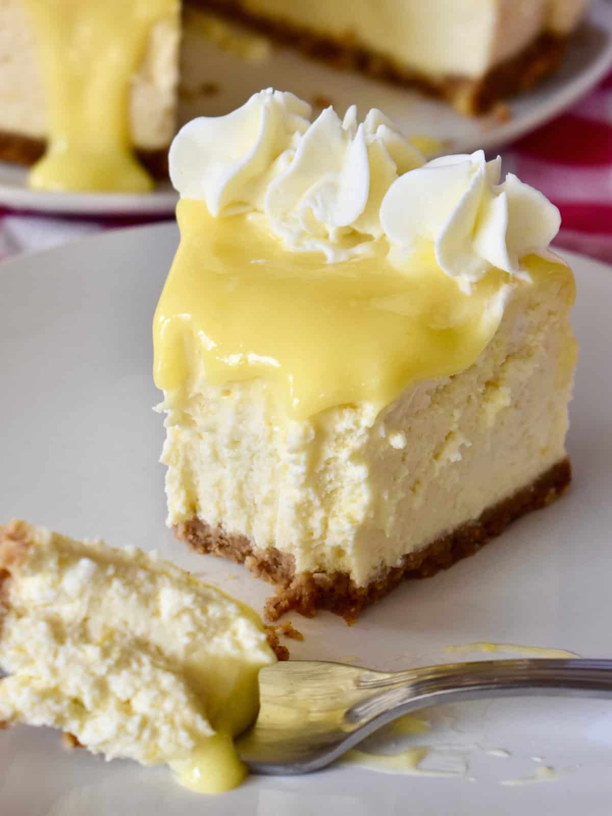 Lemon Ricotta Cheesecake slice with lemon curd topping on a white plate with fork. 
