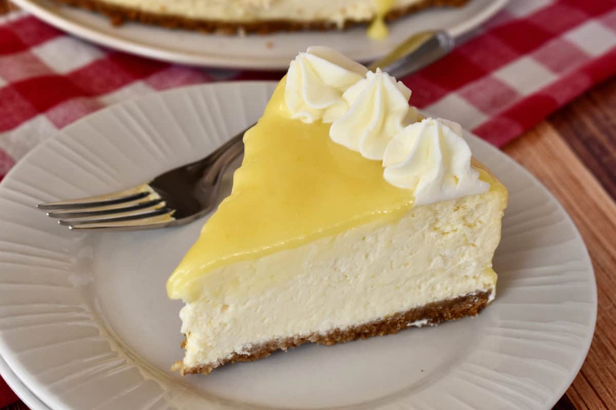 Slice of lemon ricotta cheesecake on a white plate with a fork. 