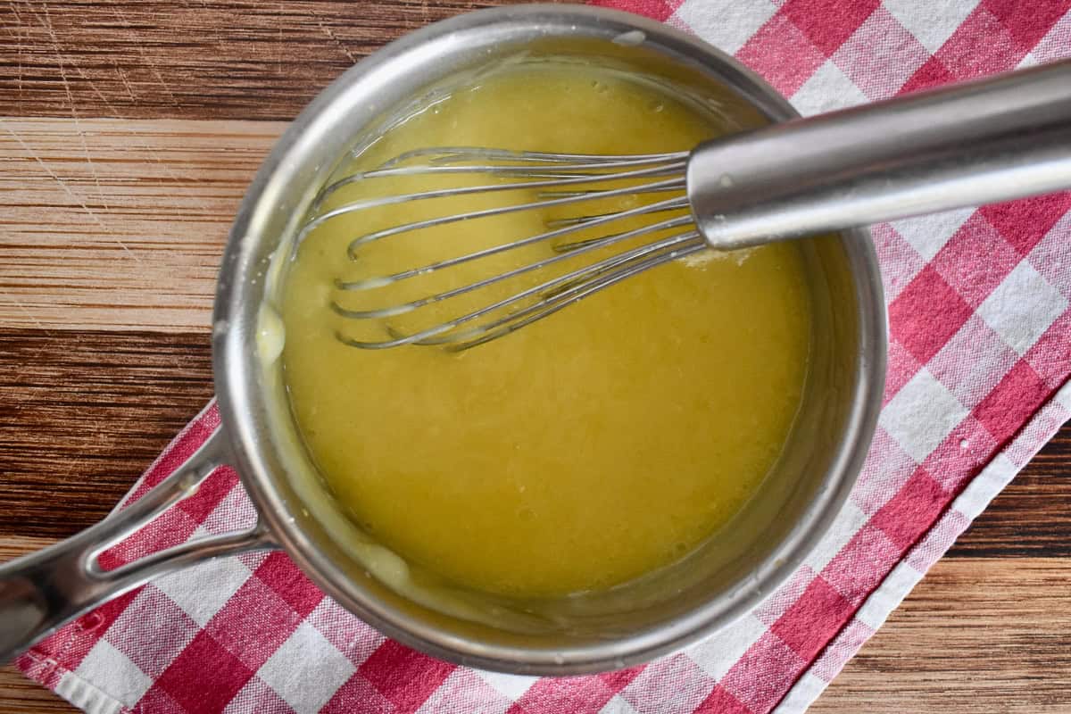 Lemon Curd cooked in a small saucepan with a whisk. 