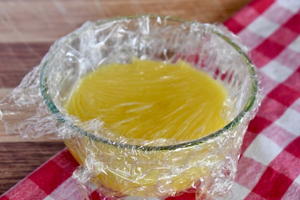 Lemon curd in a glass bowl with plastic wrap on top. 