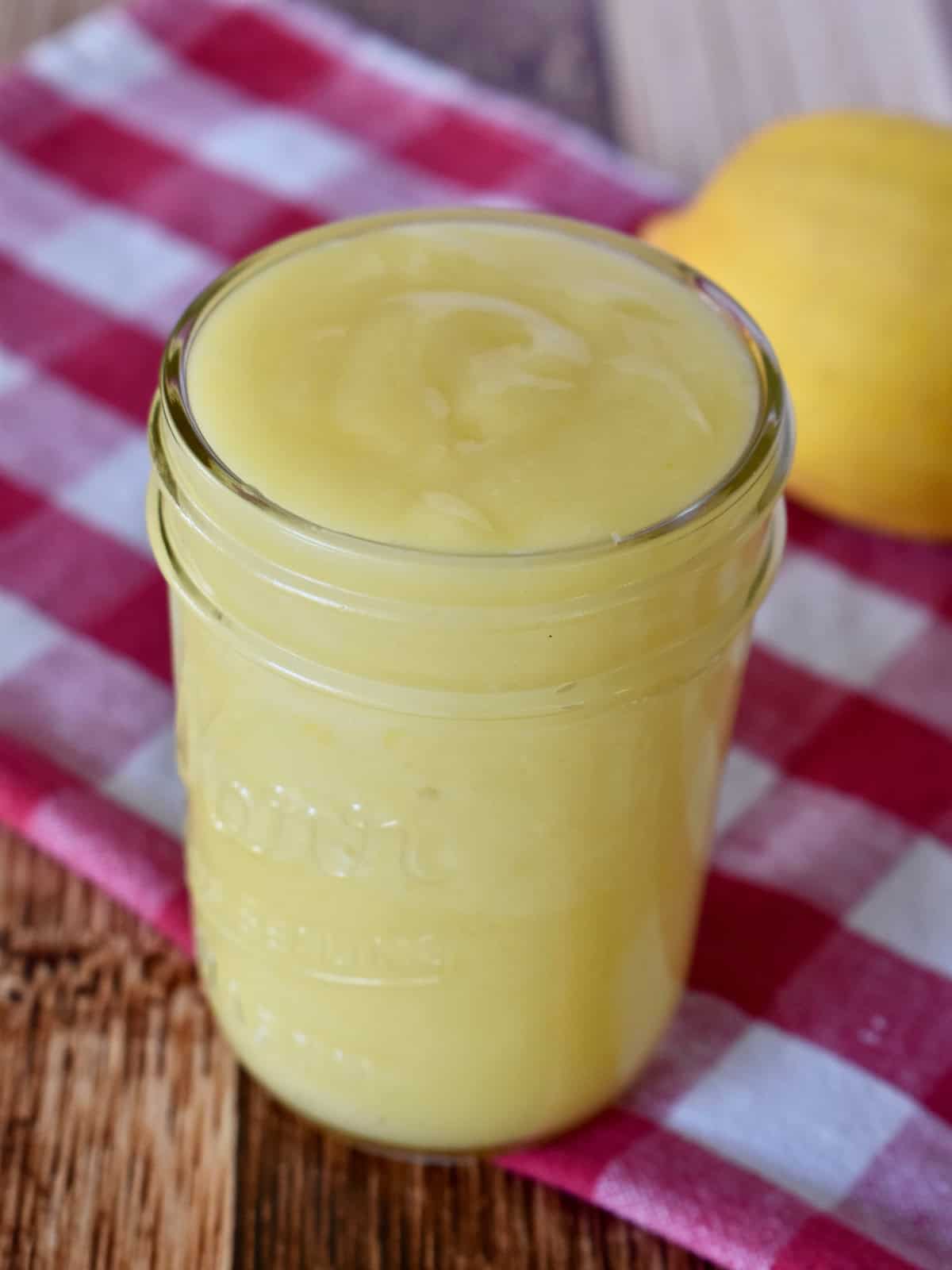 Small batch lemon curd in a jar with a lemon behind.