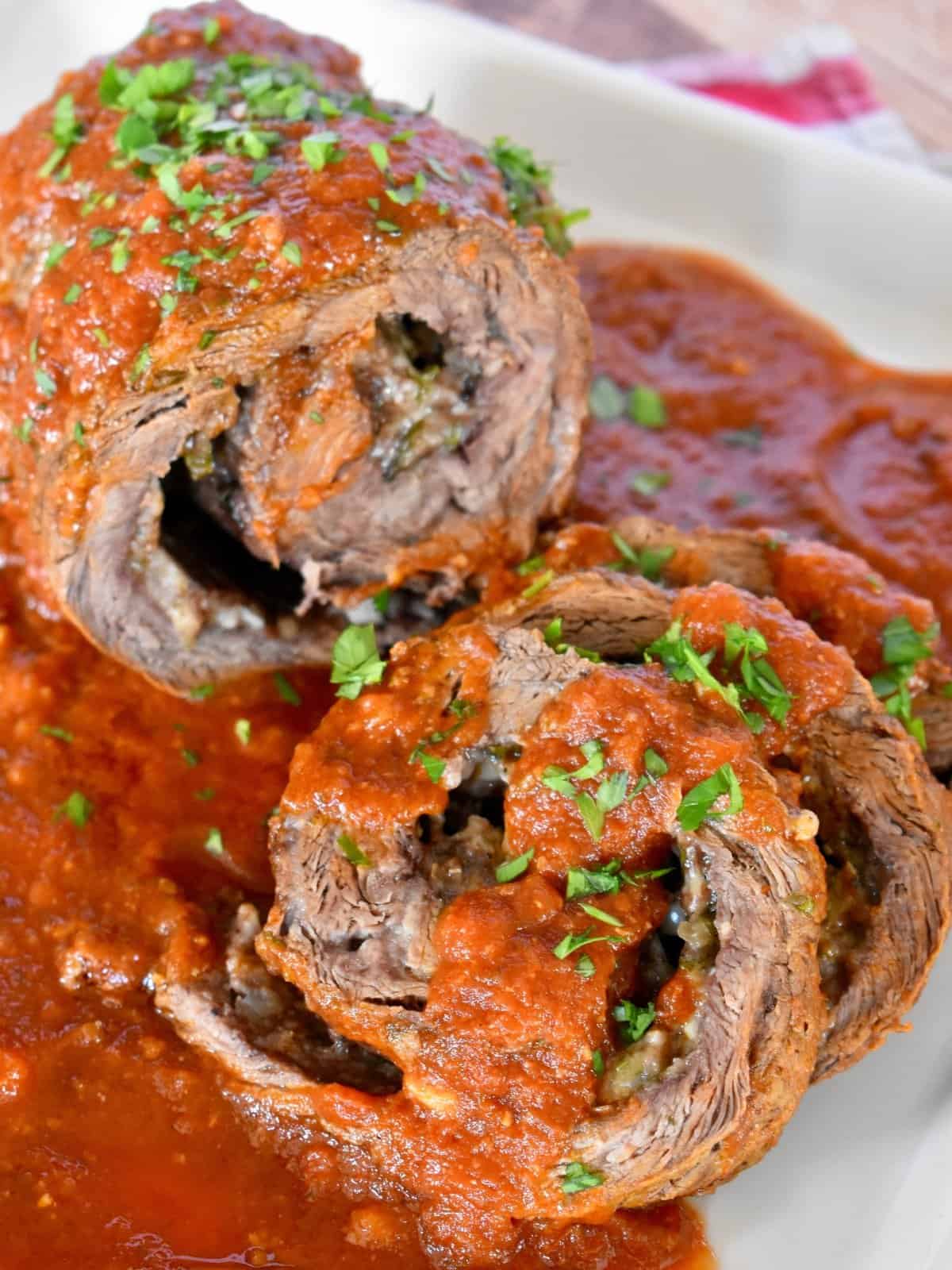 Authentic Italian Braciole on a white plate with marinara sauce spooned on top.