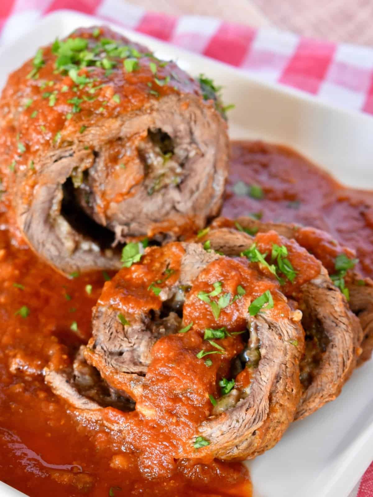 Authentic Italian Braciole sliced on a plate with marinara sauce on top. 