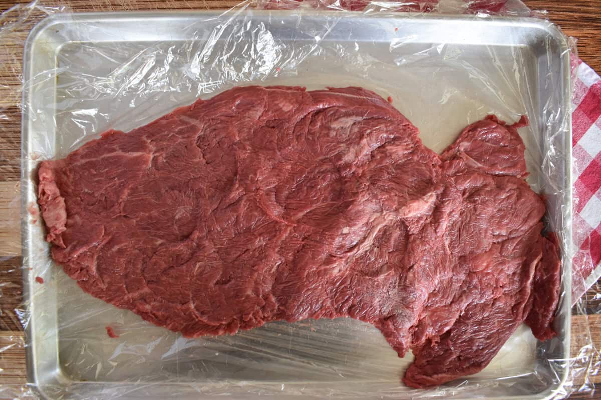 Flank steak pounded thin on a baking sheet. 